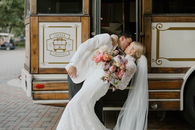 The bride and groom kissing in front of a brown and white trolley. 