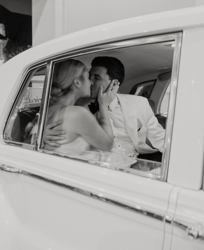 The bride and groom kissing in a white vintage getaway cat after their New Orleans-inspired wedding. 