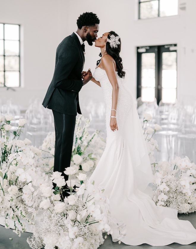 The bride and groom kissing with white florals surrounding them. 