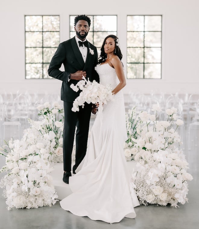 The bride and groom posing at their wedding ceremony surrounded by white florals.