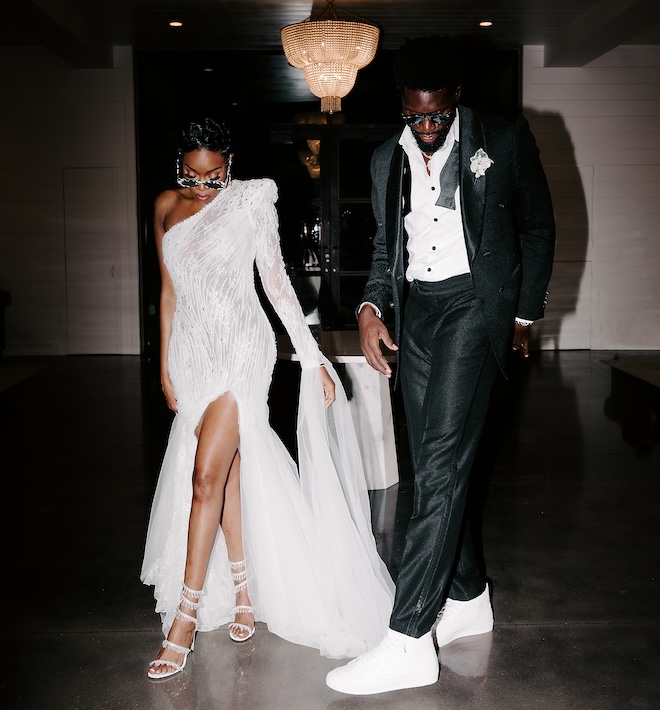 The bride and groom wearing sunglasses and looking down in their reception attire. 