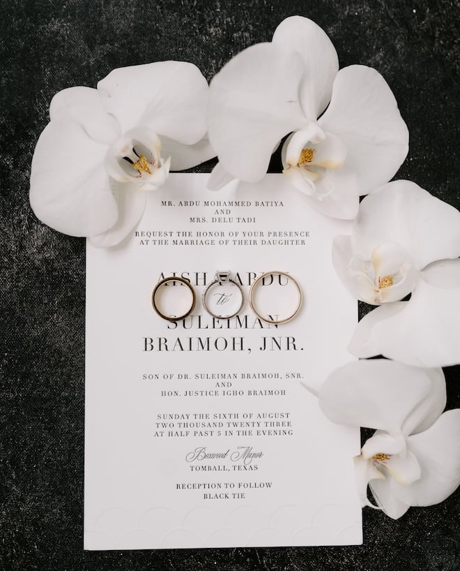 A white invitation suite with black text surrounded by white orchids. 