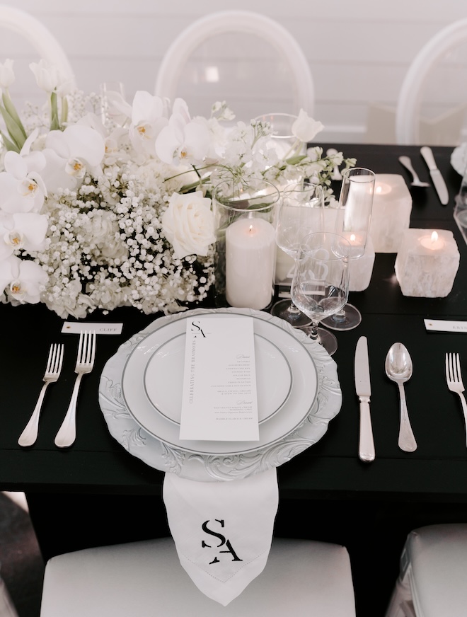 A black linen table with white plates, silverware, candles and florals. 