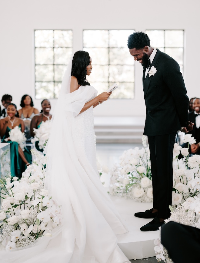 The bride reading her vows while the groom laughs. 