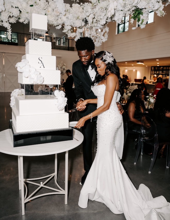 The bride and groom cutting into their white wedding cake. 