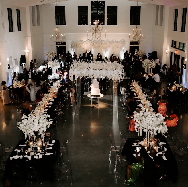 The reception space with white floral arrangements and guests walking around the space. 