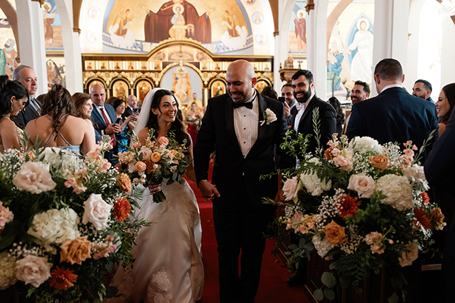 The couple hold hands as wedding guests cheer for the newlyweds.