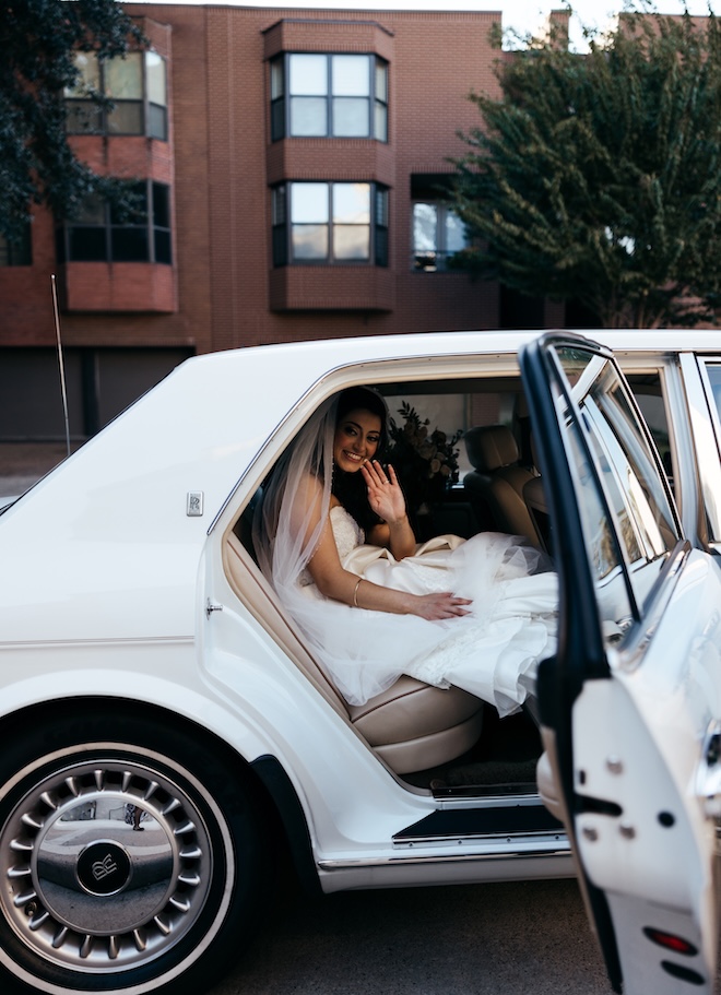 The bride waves from the inside of a white Rolls Royce. 