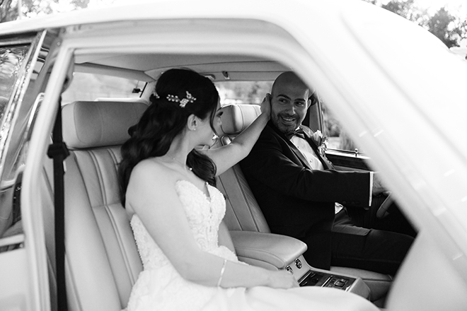 The bride and groom ride in a vintage, white Rolls Royce to their wedding reception venue. 