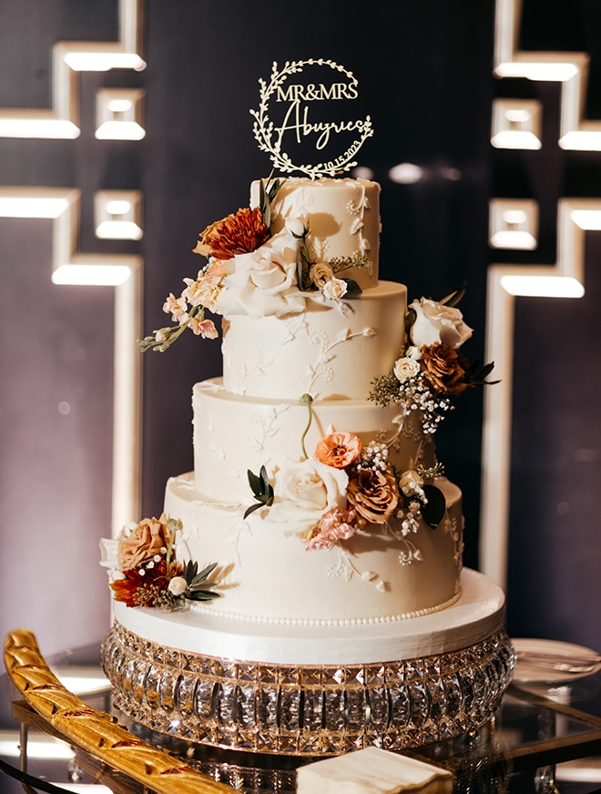 A four-tier white wedding cake is detailed in florals for the romantic fall wedding. 