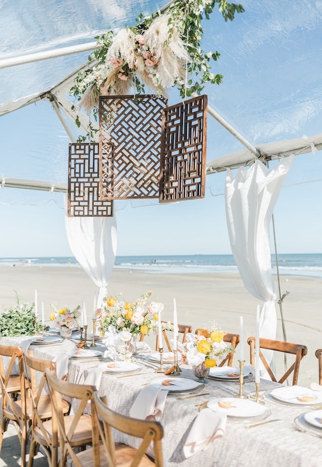 A reception table set up on a beach in Galveston Island under a tent, decorated with florals and candles. 