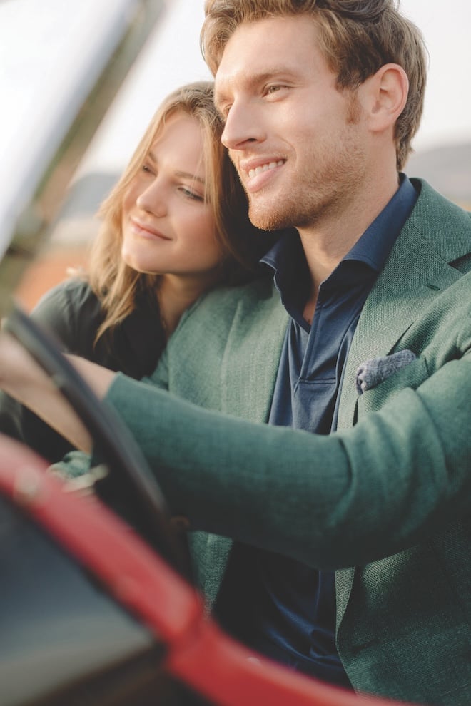 A couple smiling with the woman resting her head on the man's shoulder while driving. 