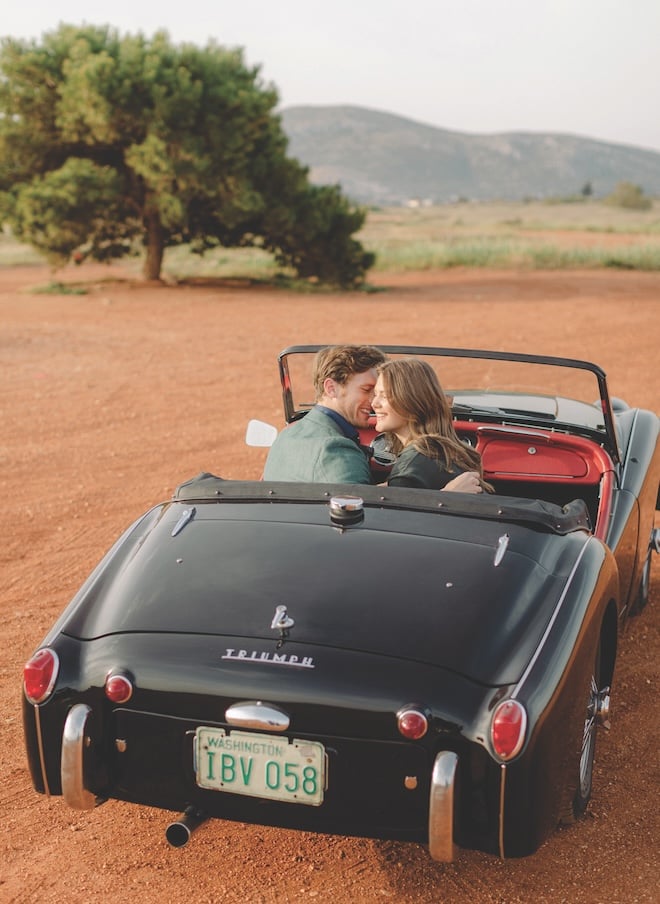 A couple smiling whole riding in a black vintage car. 