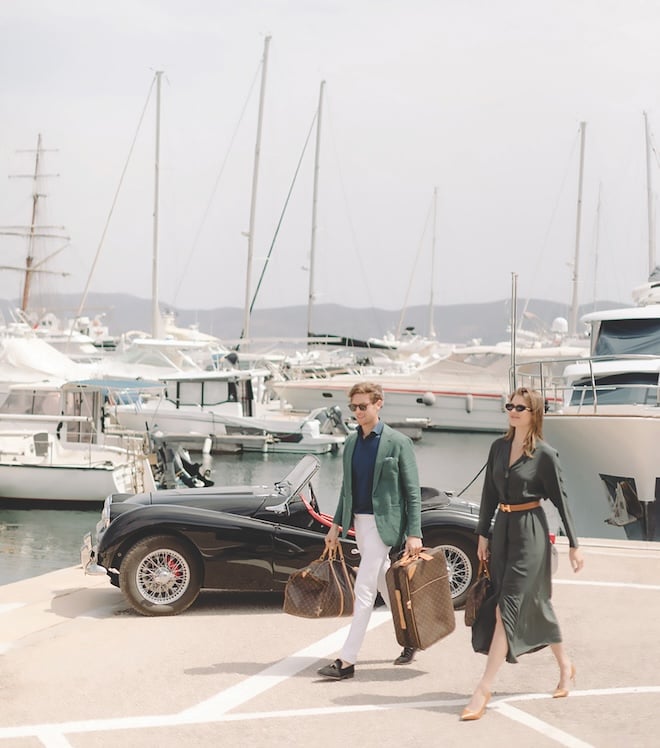 The bride and groom holding Louis Vuitton travel bags at a marina. 