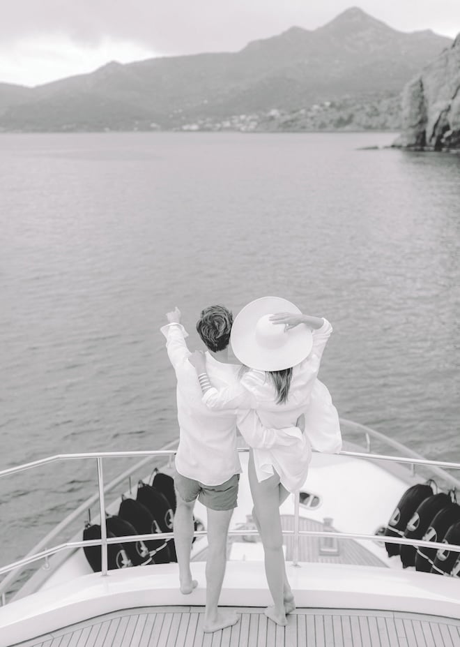 The couple looking out to sea on the front of the boat. 