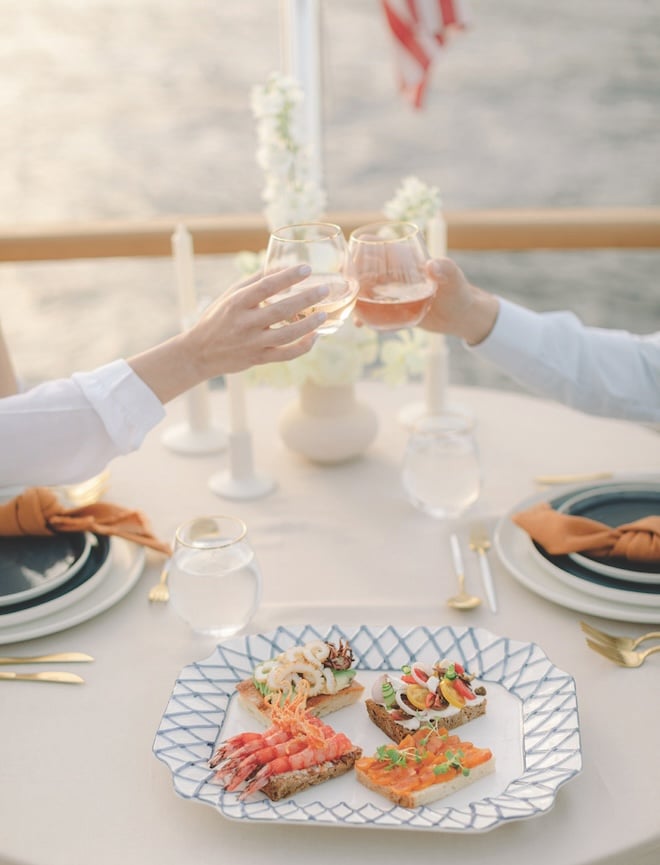 The couple clinking their wine glasses with light appetizers beneath them. 