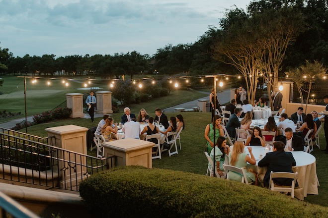 Guests sitting at round tables outside overlooking the Royal Oaks Country Club golf course, for a New Orleans style wedding reception.