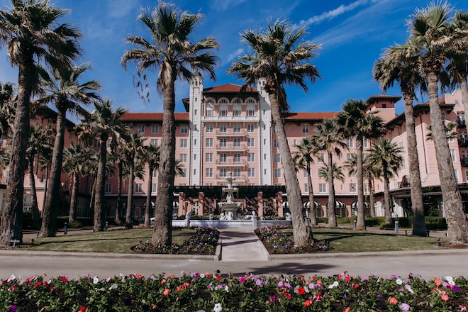 The exterior of Grand Galvez, the large pink hotel with palm trees in the lawn. 