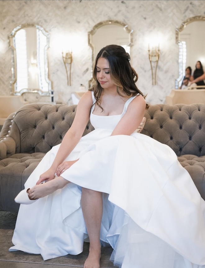 The bride puts on her wedding shoes while getting ready. 