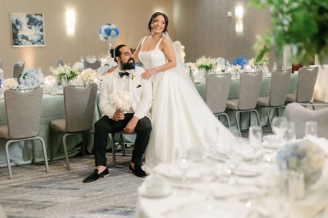 A bride and groom smiling in the ballroom of the JW Marriott Houston by the Galleria decorated with white and blue florals. 