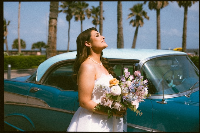 he bride holds her wedding bouquet while standing in front of a blue vintage car.