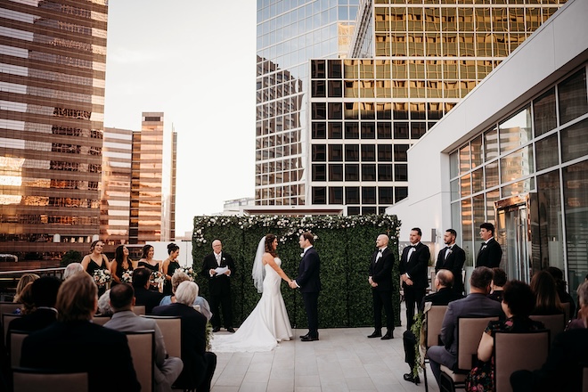 A bride and groom holding hands during their wedding ceremony on the terrace of the Westin Houston Medical Center/Museum District. 