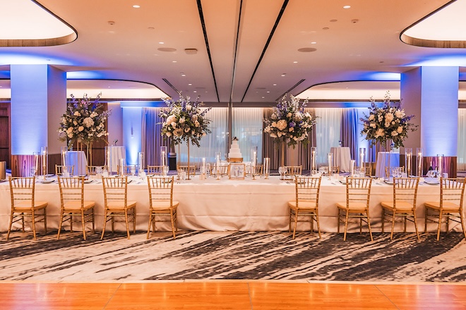 The ballroom of Four Seasons Hotel Houston decorated with a long reception table, floral centerpieces and a white cake. 