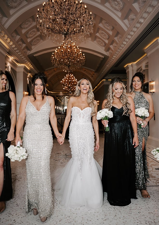 The bride and her bridesmaids laugh and smile while walking. 