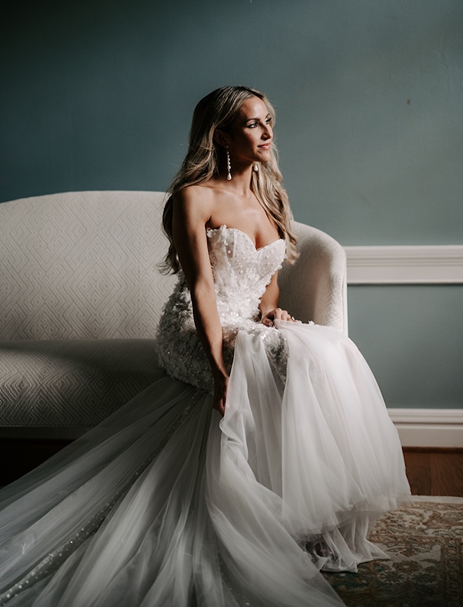 The bride sits on a couch wearing her wedding dress.