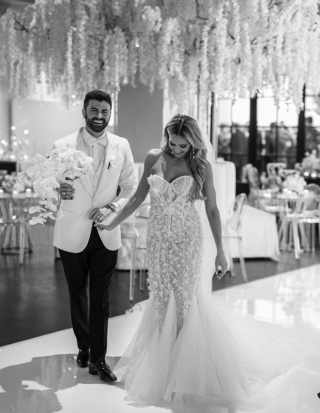 The bride and groom hold hands as they walk through their reception venue, Le Tesserae. 