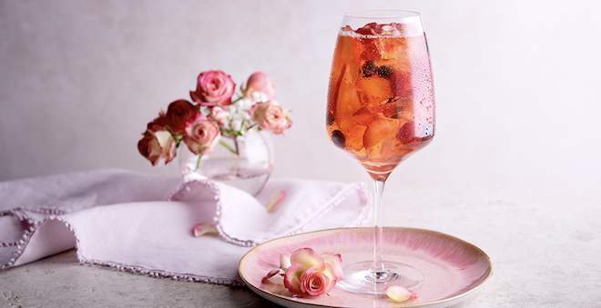 A pink cocktail on a pink plate with pink florals behind it. 