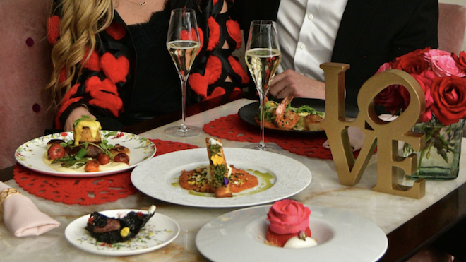 A couple at a table with two Champagne glasses and an array of food in front of them. 