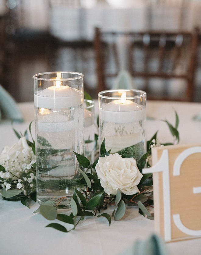 Candles and greenery decorate the reception tables at the sage green and white wedding reception. 