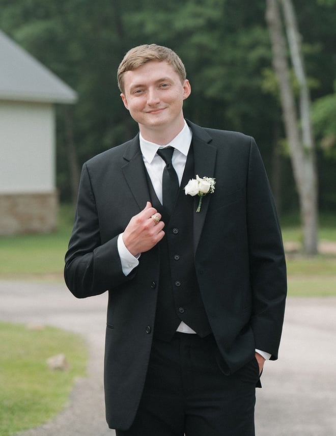 The groom wears a suite with a white rose and baby's breath boutonniere.