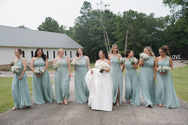 The bride and her bridesmaids walk outside the wedding venue wearing their dresses and holding their bouquets. 