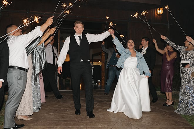 The bride and groom hold hands under a sparkler send-off from their wedding reception. 