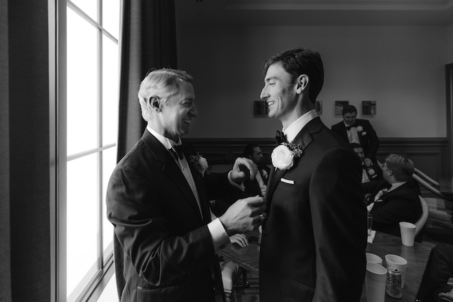 The groom laughing with a man in the wedding party. 