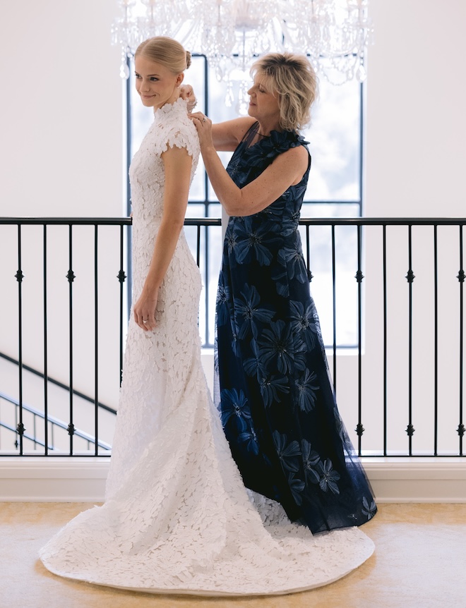 The brides mom buttoning the back of the bride's all lace short-sleeved wedding gown. 