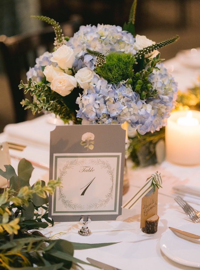 Blue and green floral arrangements with a table number in front. 