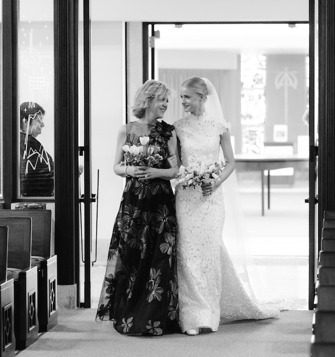 The bride and her mother smiling at each other as they walk down the aisle. 