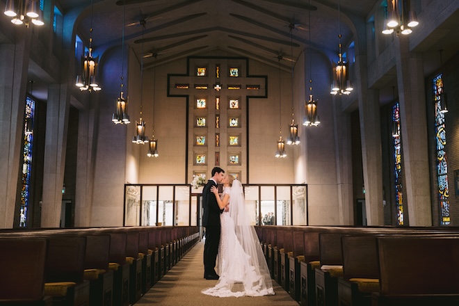 A bride and groom standing in the aisle of the church kissing. 