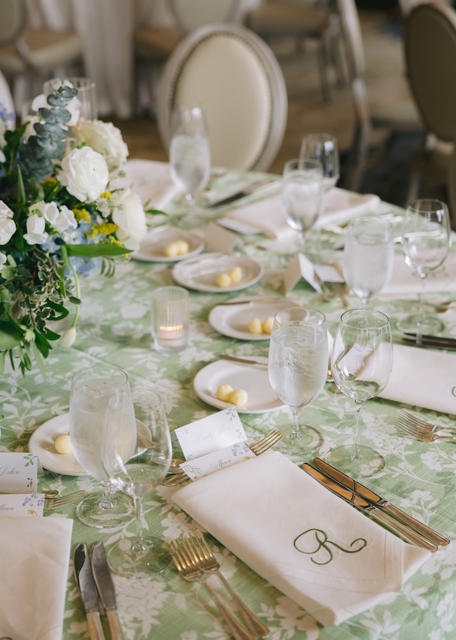 The tablescape with green printed linens, monogrammed napkins, and a floral centerpiece. 