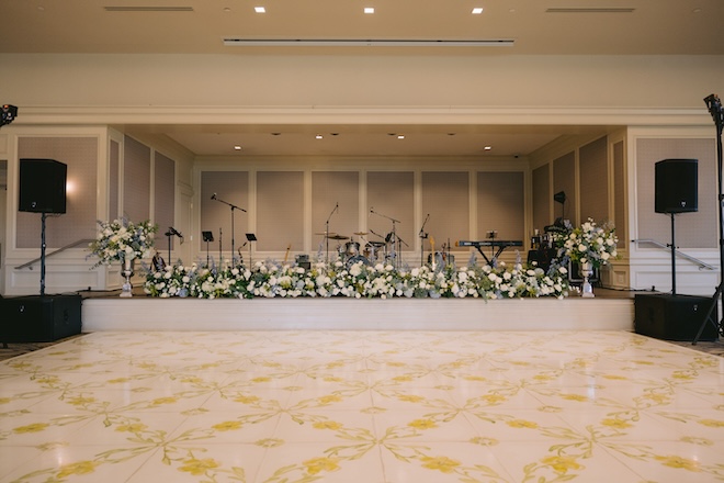 A yellow and white floral print dance floor in front of a stage covered in white and blue florals. 