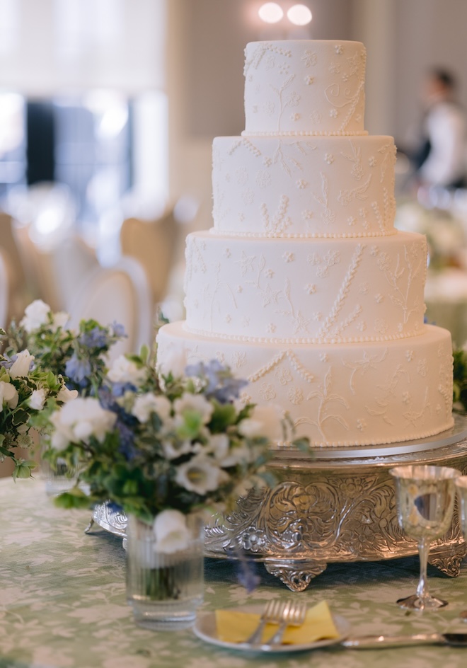 A four-tier white wedding cake with floral embossments. 