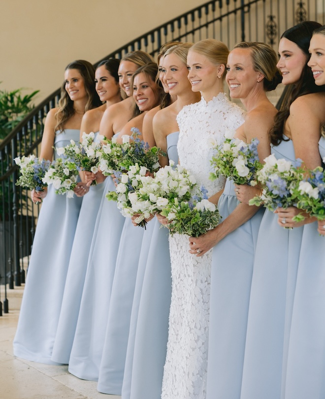 The bride smiling with her bridesmaids in strapless blue gowns and white and blue bouquets. 