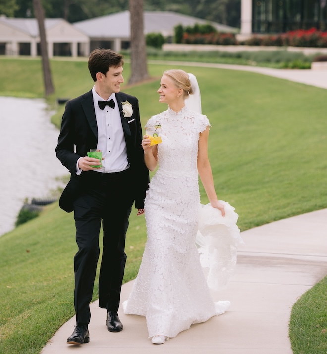 The bride and groom holding cocktails while walking along the greens of the country club. 