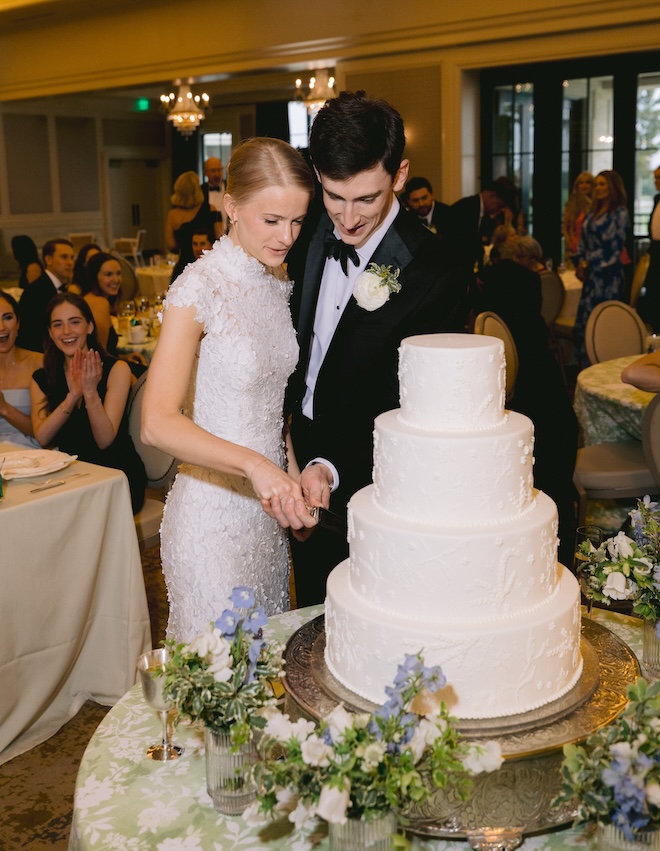 The bride and groom cutting the four tier white wedding cake. 