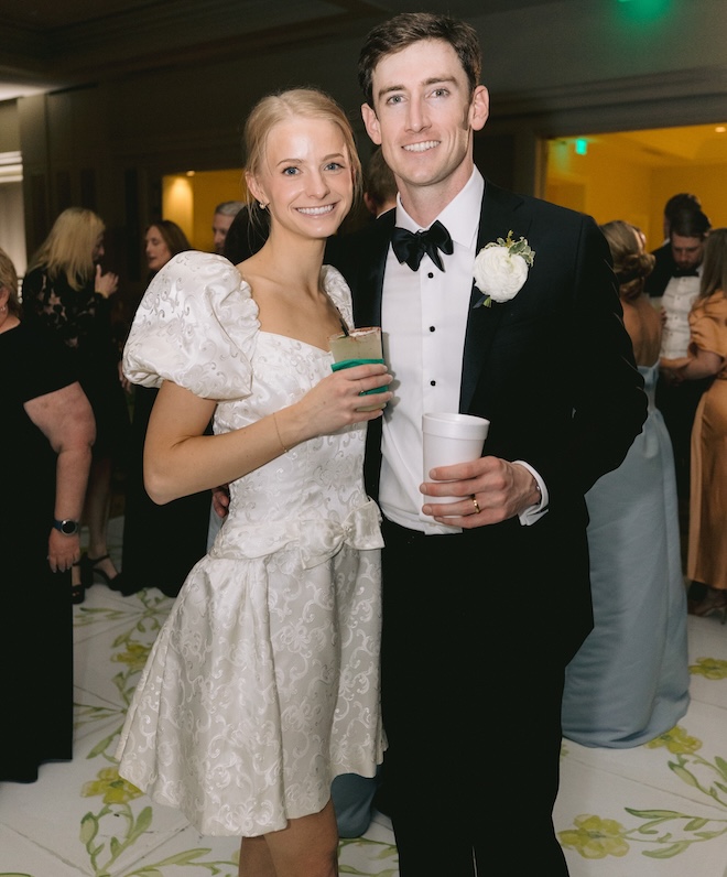 The bride and groom holding drinks and the bride is wearing a short wedding gown that looks vintage. 