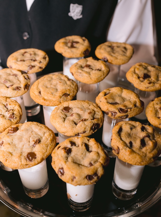 Chocolate chip cookies resting on shot glasses of milk. 