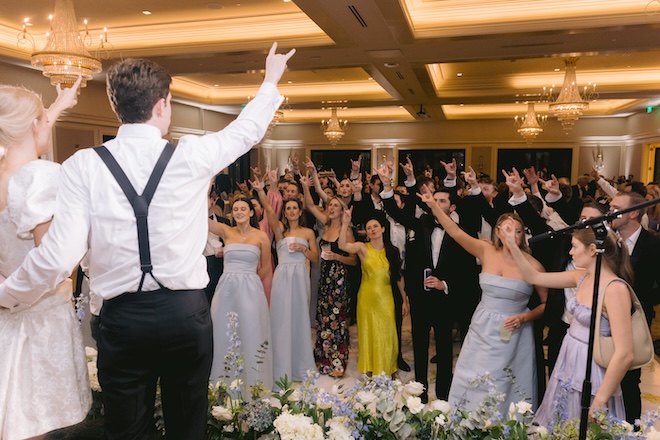 The bride and groom standing on the stage with their hook em' horns hand symbol with guests doing it back to them. 